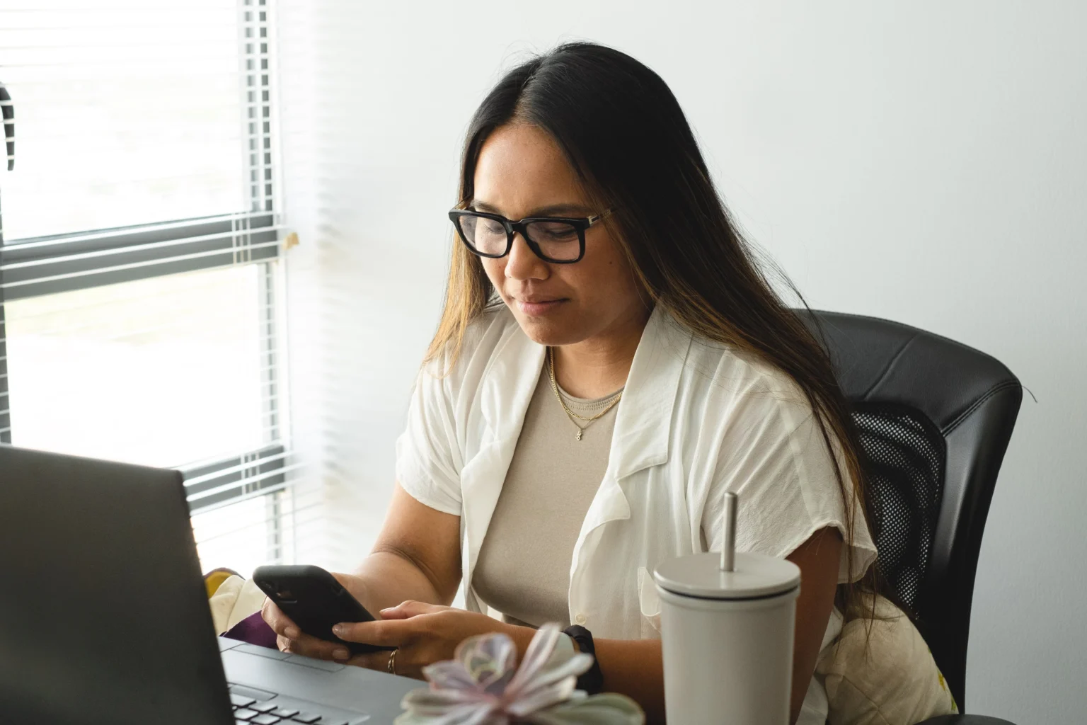 Mujer trabajando simultáneamente con un teléfono móvil y un ordenador en un entorno profesional.