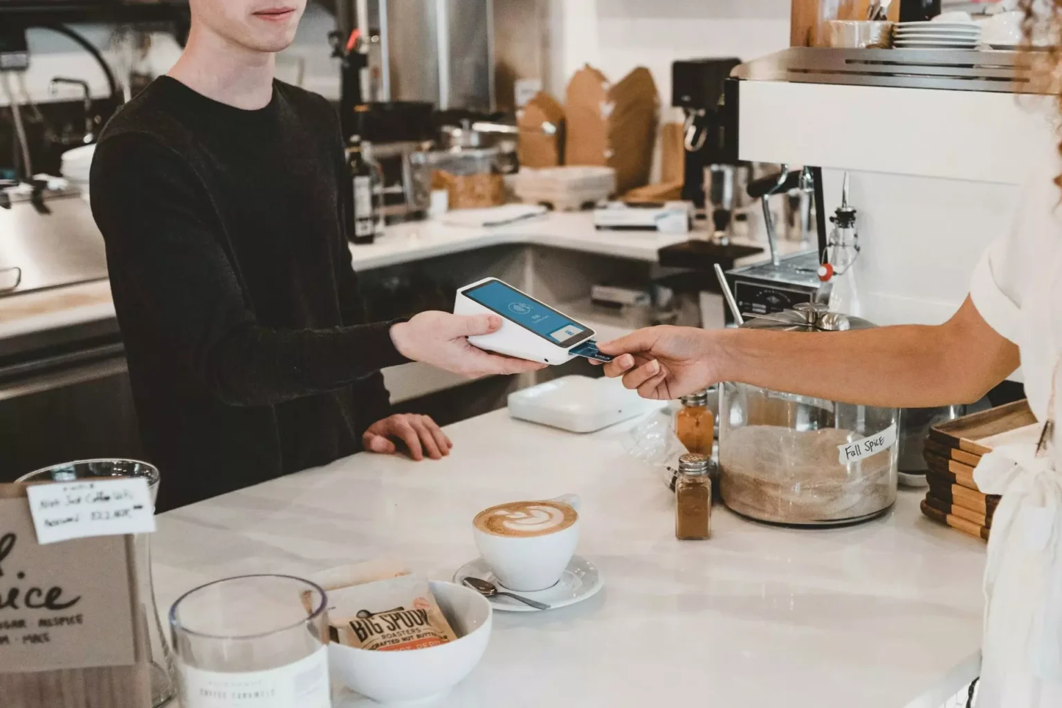 "Joven realizando un pago con tarjeta en un datáfono dentro de un bar.”